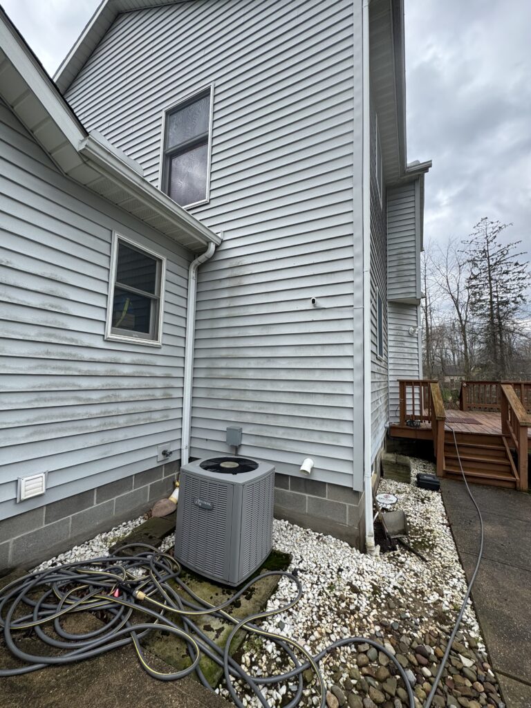 Outdoor HVAC compressor unit beside a light-blue siding house with numerous hoses scattered on white gravel.