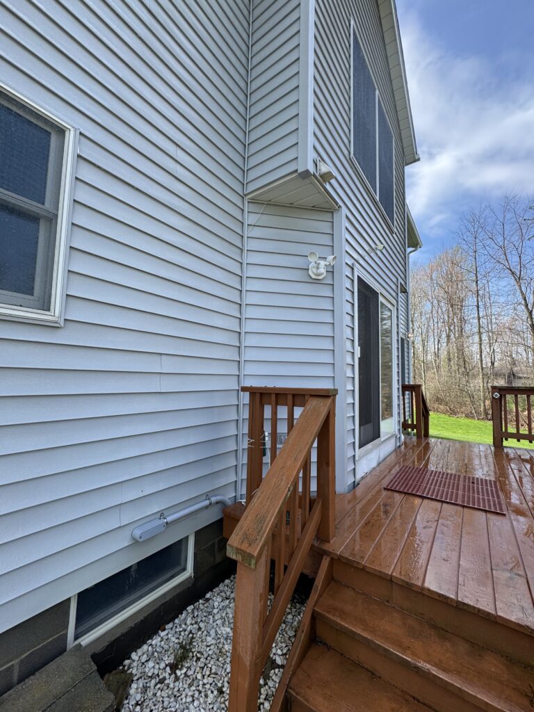 Wooden deck stairs along the side of a blue house with vinyl siding and a small overhang above the door.