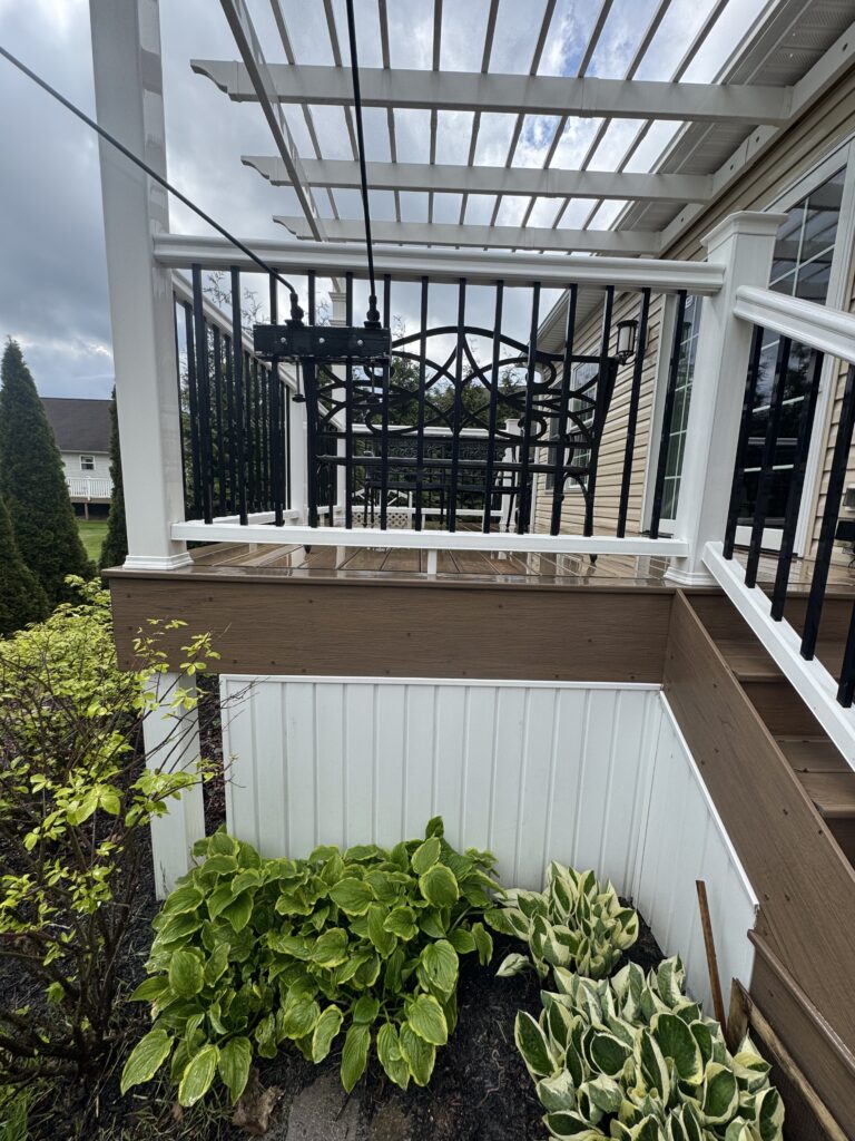 Hosta plants with green leaves edged in yellow in a garden bed beside a white railing and wooden deck.