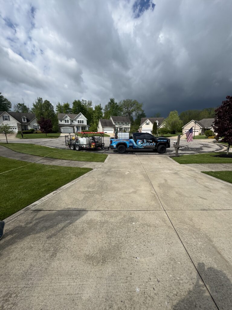 Suburban street with a blue service truck and equipment trailer parked in a cul-de-sac as dark storm clouds approach.