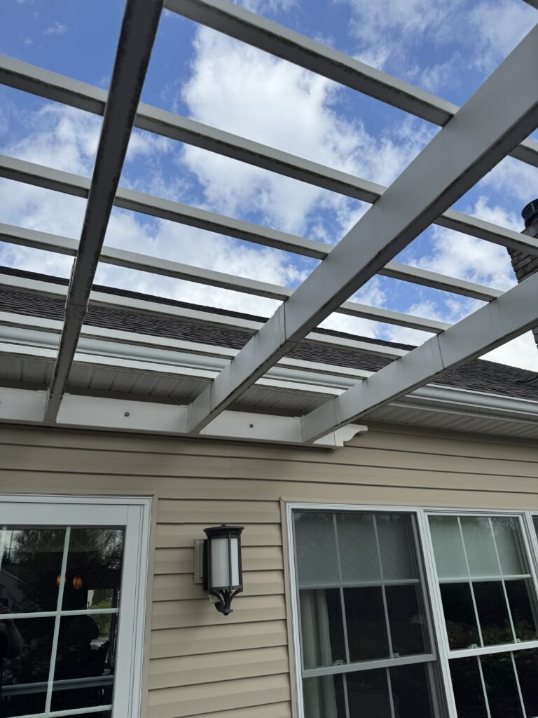 White pergola framing over a beige house with large windows, against a blue sky with clouds.