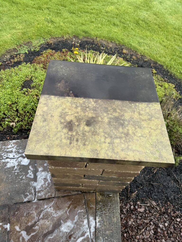 Weathered flat lid on a stacked wooden beehive in a garden, with green lawn nearby.