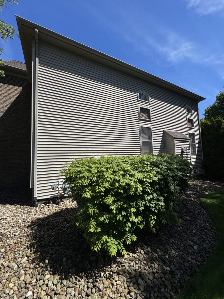 Exterior view of a multi‑story house with gray siding, arched windows, and landscaped rock bed under a blue sky
