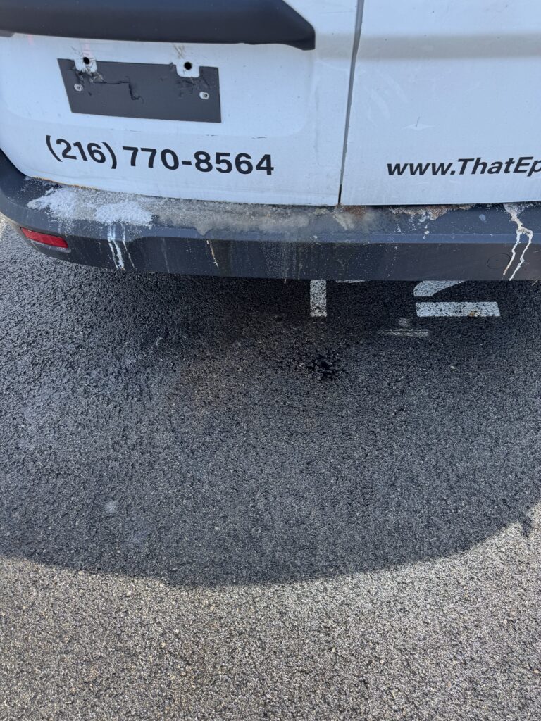 Back of a white van with a damaged license-plate area, showing the phone number (216) 770-8564 and part of the URL www.ThatEp on the side; dirt and mud along the bumper.