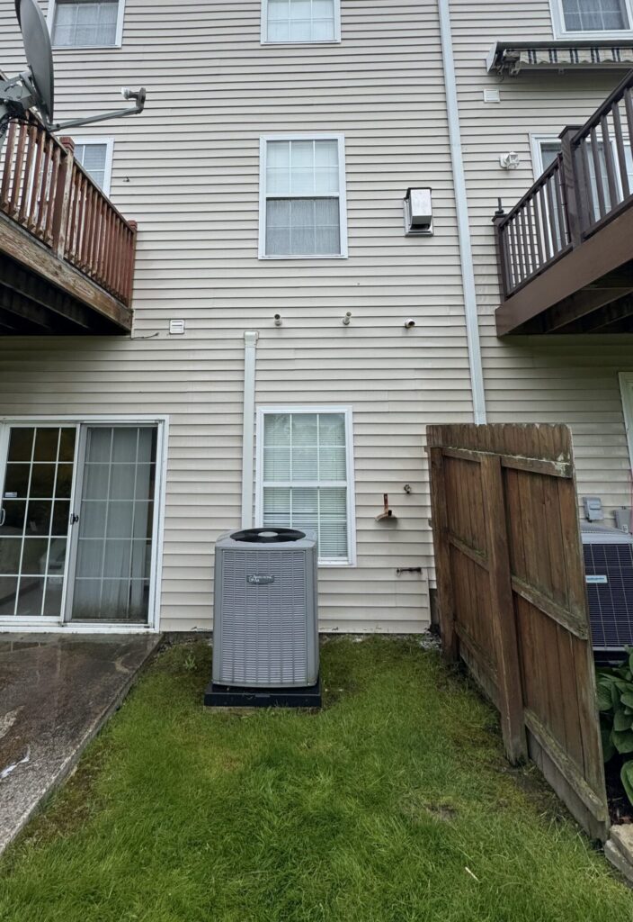 Backyard view of a beige townhouse rear: deck with satellite dish, sliding glass door, and a central air conditioner on the lawn.