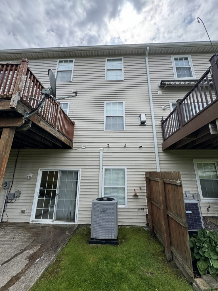 Backyard of a beige townhouse with a satellite dish on the left deck and sliding glass door on the ground level.