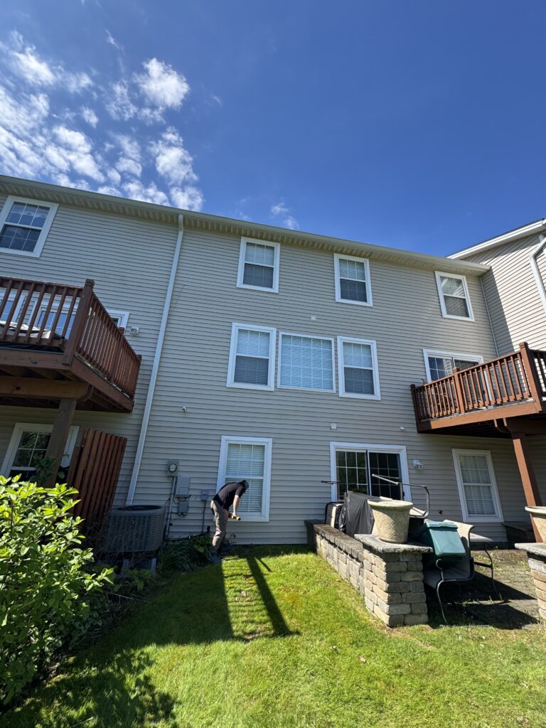 Backyard of a beige townhouse with white-framed windows and two wooden decks; a person kneeling near a back door in the yard.