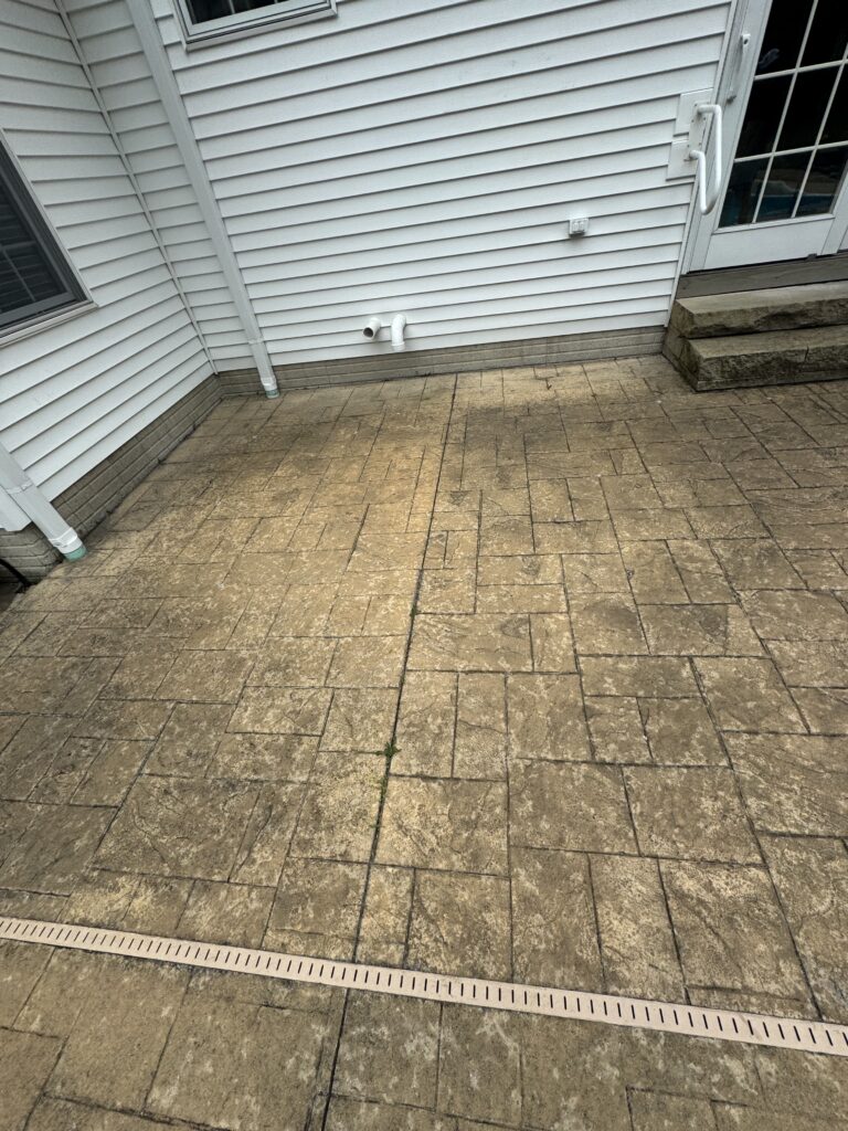 Backyard patio with beige stamped concrete, white vinyl siding, a glass door, steps, and two PVC pipes protruding from the wall.