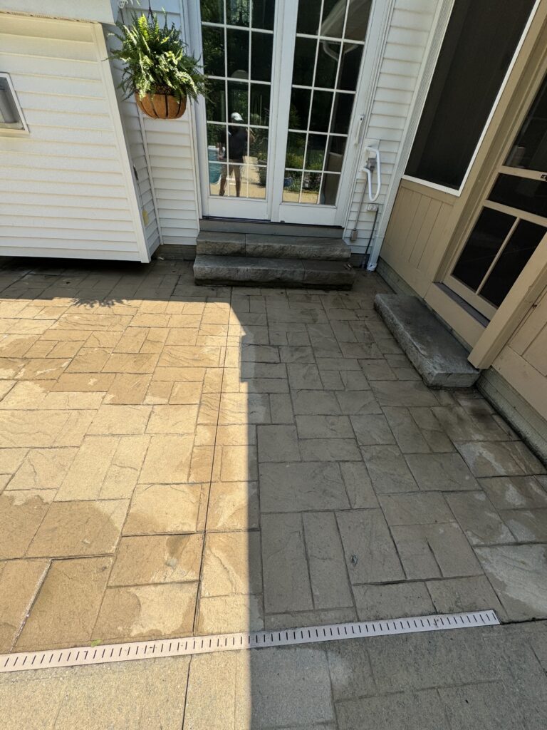 Patio area with two-step stone stairs leading to white-framed glass doors, a hanging fern planter above, and a long measuring ruler across beige pavers.