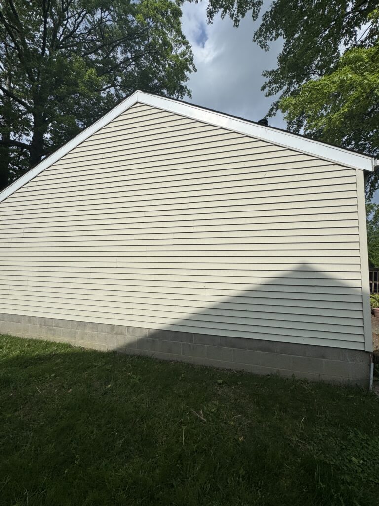 Beige clapboard house wall with white trim and a concrete block foundation; trees and sky above.
