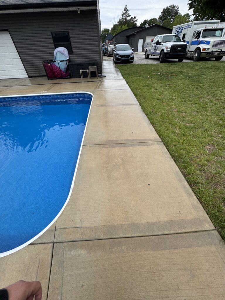 Backyard scene with a blue in-ground pool along a concrete patio; several trucks parked on the grass in the background.