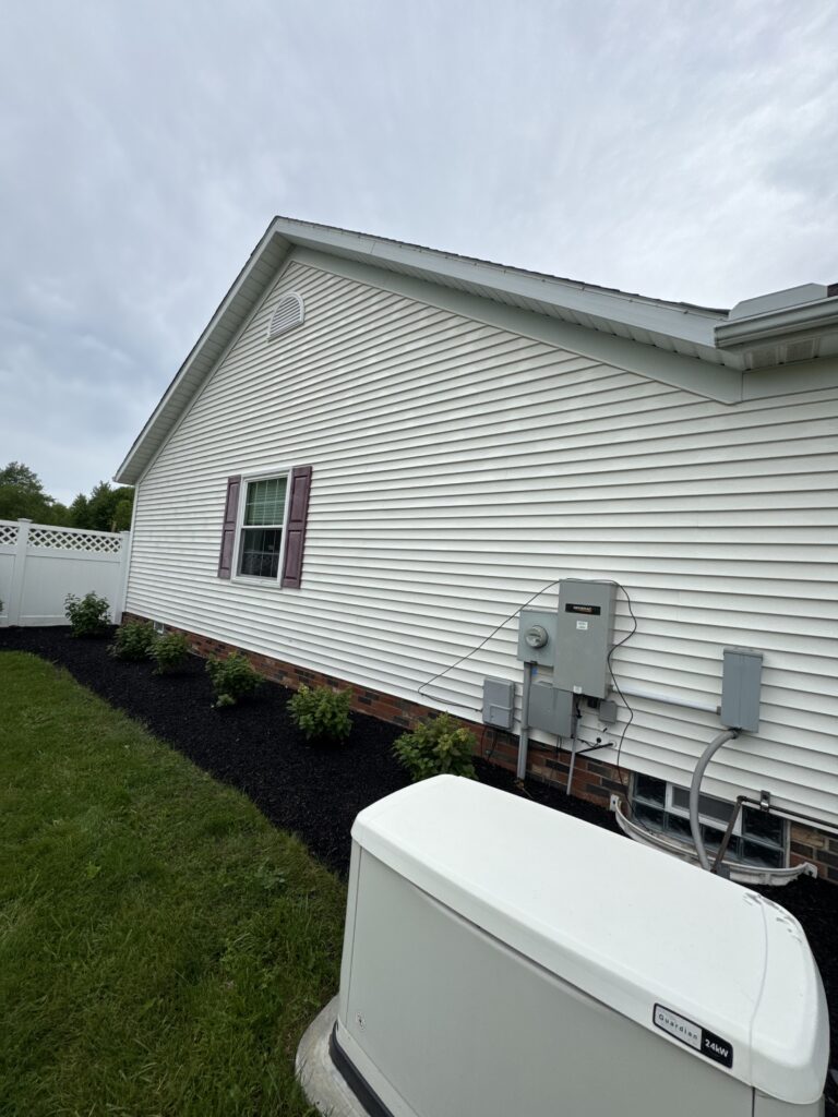 Side of a white vinyl-sided house with a small window and purple shutters, a vent in the gable, and a gray generator by the foundation.