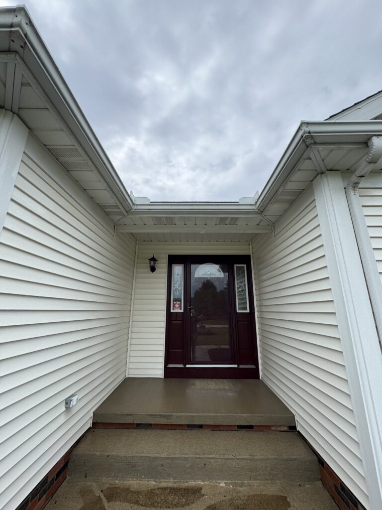 Covered front entry with a small porch, white siding, and a dark red door beneath an overcast sky.