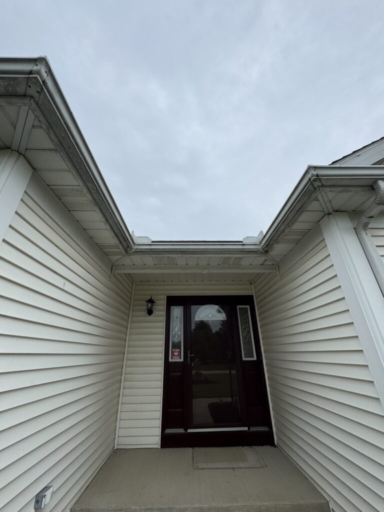 Front entryway of a house with white siding and a dark door at the top of a small concrete porch stairs under a covered entryway on a cloudy day