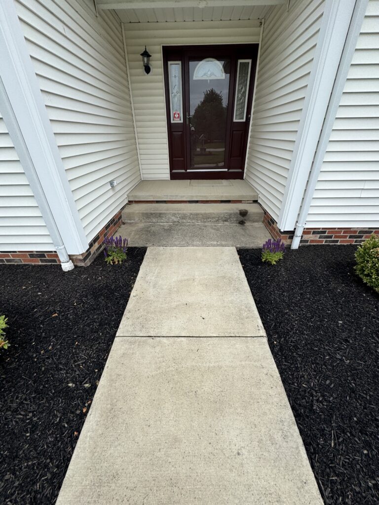 Front entry with a maroon door and decorative glass panels, small porch, and exterior beige siding. Light fixture to the left and concrete steps leading to the door.