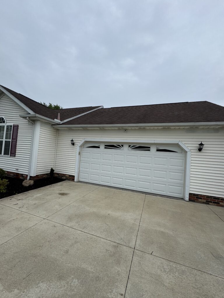 White siding house with a two-car garage, maroon shutters, and a cloudy sky overhead.