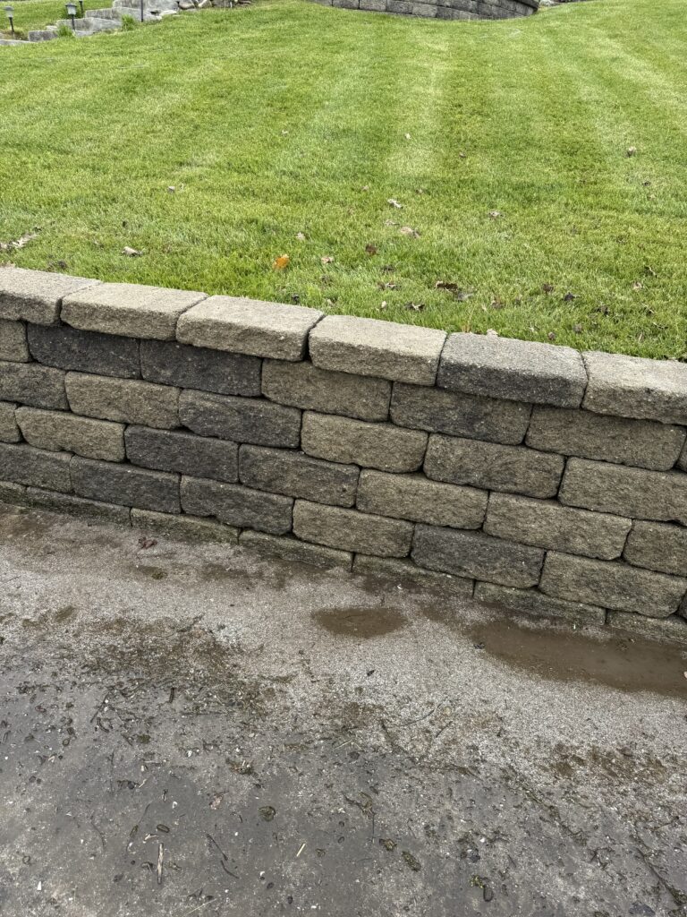 Stone block retaining wall beside a well-kept grassy lawn; a damp concrete path is in front of it.
