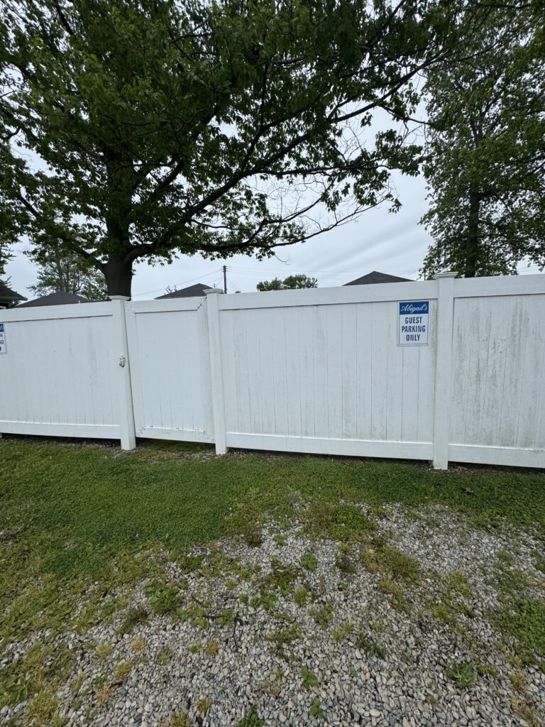 White vinyl fence with a blue Abigail's Guest Parking Only sign, gravel and grass in the foreground, and a tree canopy above.
