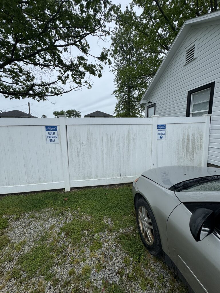 White privacy fence with 'Guest Parking Only' and 'Parking for Cottage 2' signs, and a gray car parked beside a white house.