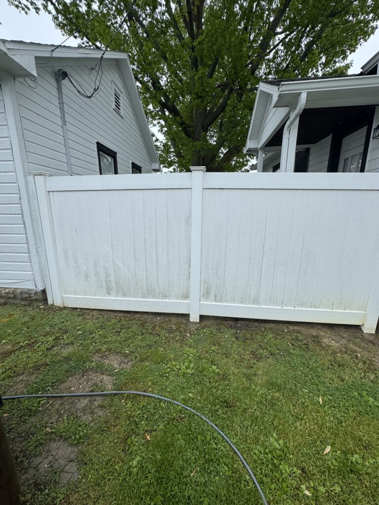 White privacy fence between two white houses, with a large leafy tree in the background across the yard.