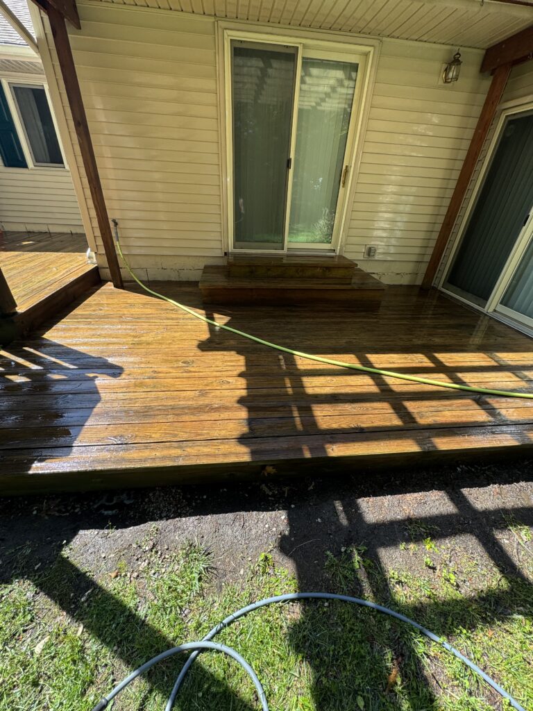 Backyard deck with a sliding glass door, wooden steps, and a green hose curling across wet planks.
