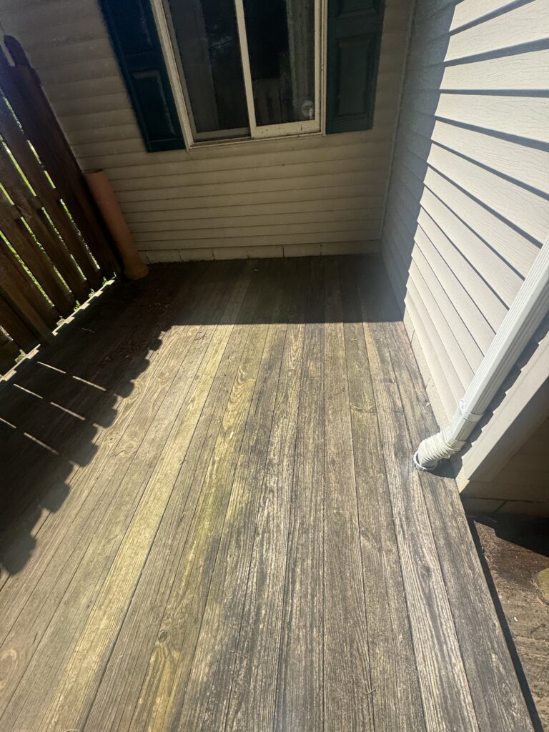 Wooden balcony deck with beige siding, a small window with dark shutters and a drainpipe along the wall.