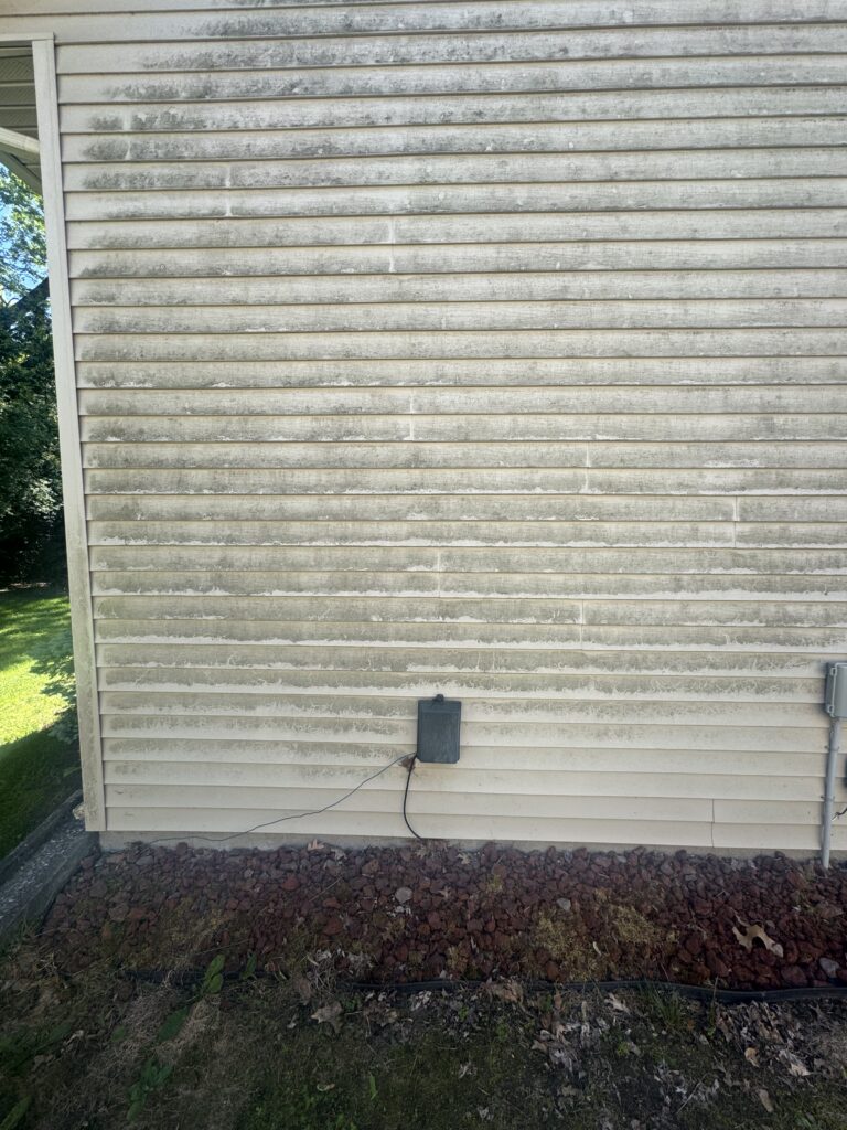Exterior wall of a house with beige horizontal siding, a small gray electrical box mounted near the base, and cables running along the ground.
