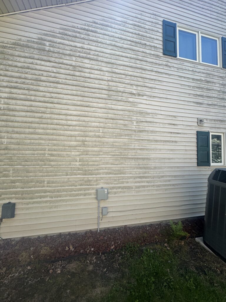 Exterior wall of a house with beige siding, blue shutters, and windows; utility boxes mounted on the wall and an outdoor unit visible in the corner.