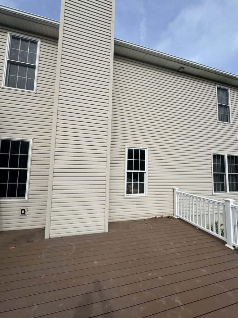 Beige siding house exterior with several white-framed windows and a wooden deck with a white railing.