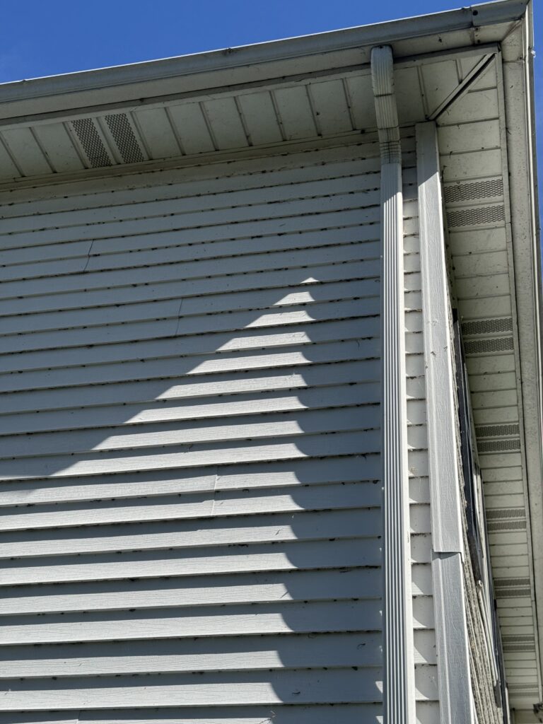Close-up of white horizontal siding, gutter, and downspout on a house with a bright blue sky above.
