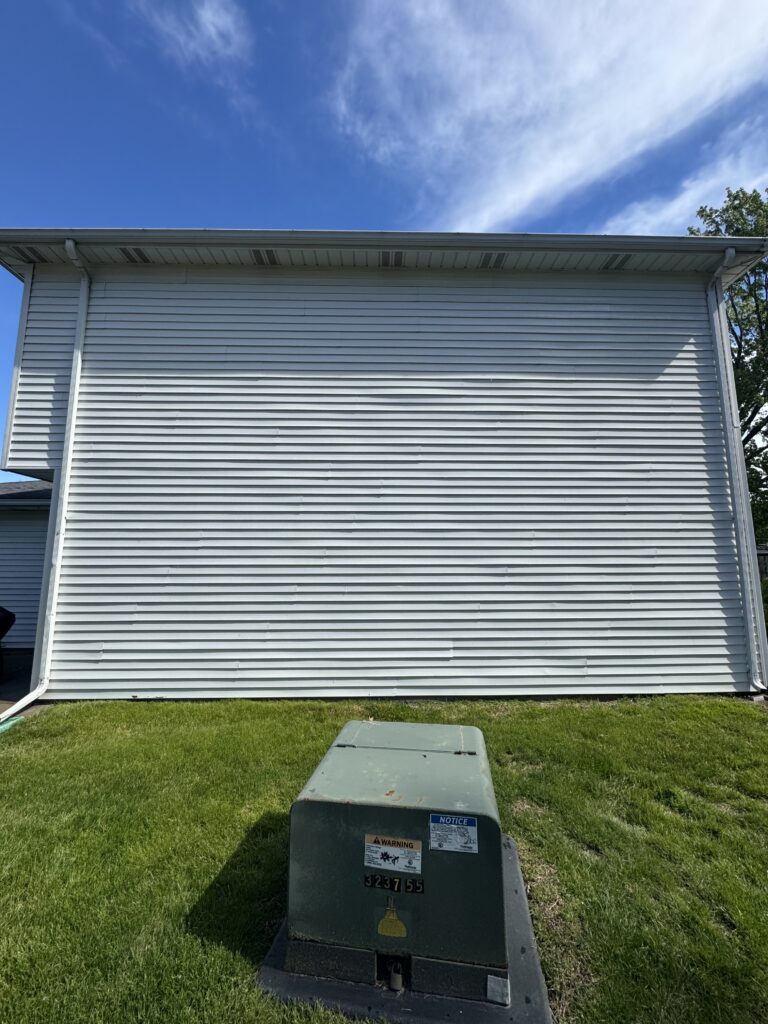 Electrical transformer box in a grassy backyard in front of a white siding building against a bright blue sky.