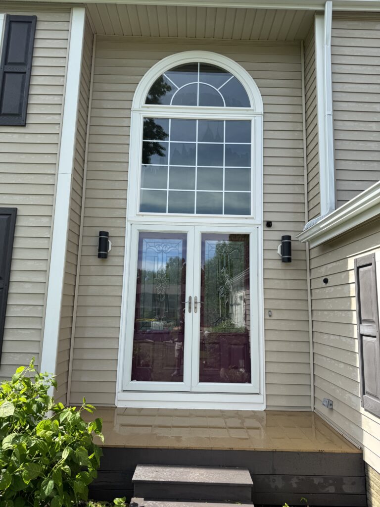 White-framed double doors with an arched window above, set in beige siding, small front porch and steps.