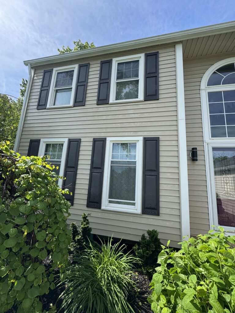 Beige two-story house with white-trimmed windows and dark blue shutters, front garden in foreground.