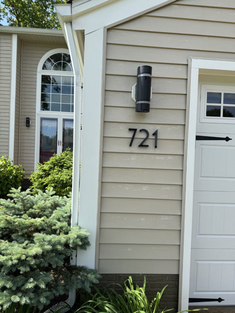 Exterior of a beige house with white trim, showing a curved arched window and a black wall-mounted light fixture beside the address 721.