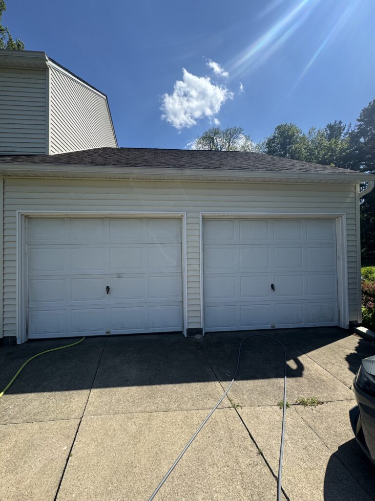 Two-car garage with white panel doors, beige siding, and a sunlit blue sky above.