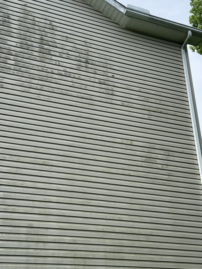 Exterior wall with horizontal gray vinyl siding, a metal gutter and downspout along the right edge; minor dirt streaks on the siding.