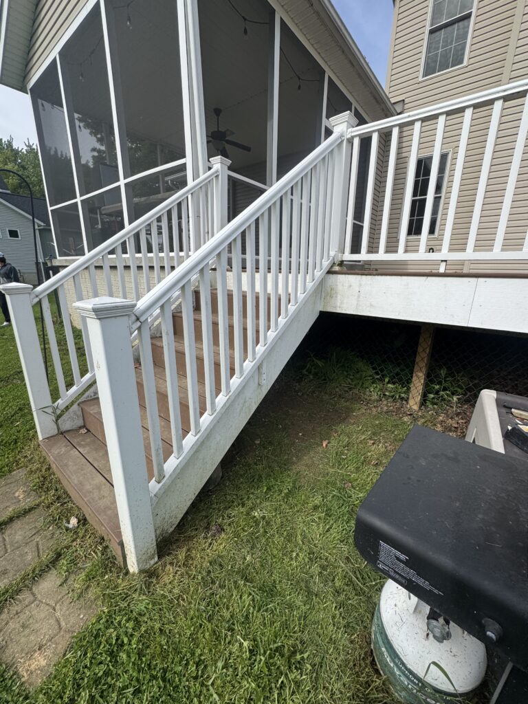 White railing-led staircase to a screened porch on a beige house, with a ceiling fan visible inside.