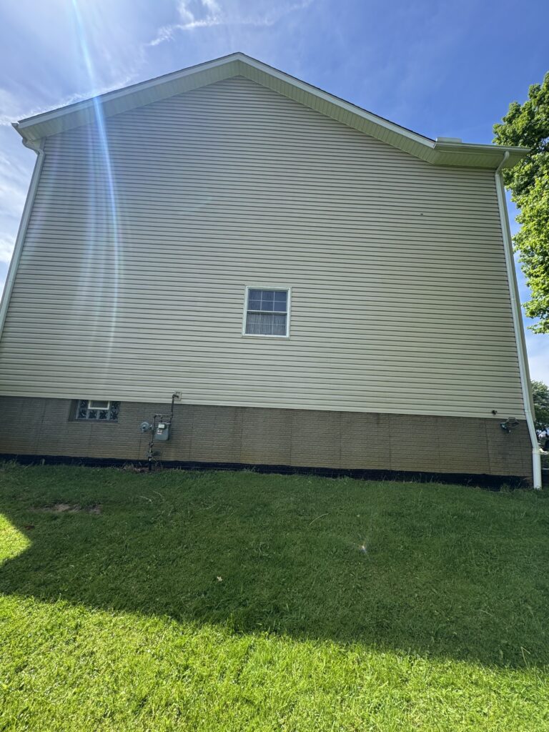 Rear side of a beige vinyl-siding house with a small square window and green lawn in the foreground.