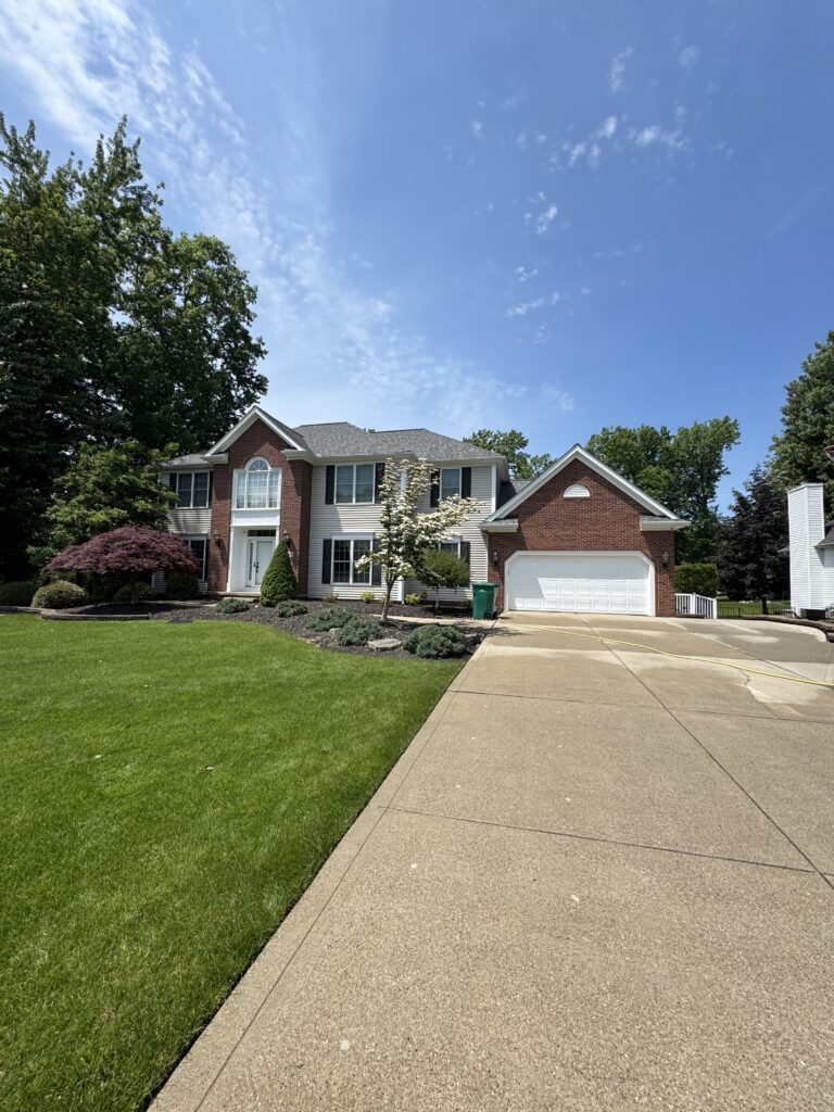 Two-story brick-and-siding suburban home with a white-trimmed front door, attached two-car garage, and a manicured lawn under a clear blue sky.