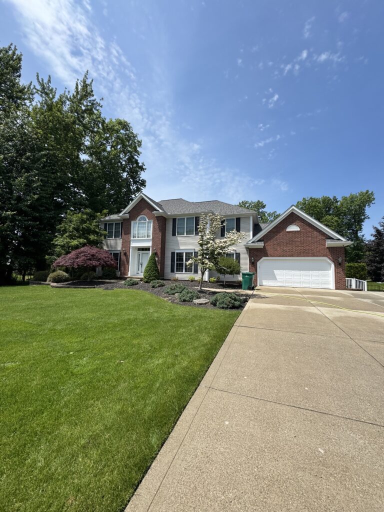 Two-story brick-and-siding house with an attached two-car garage, manicured lawn, and blue sky.