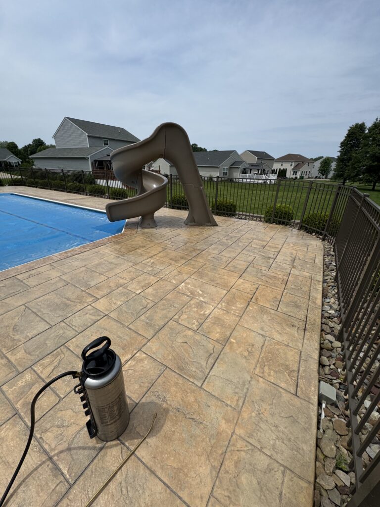 Brown twisting backyard pool slide beside a rectangular blue pool, with a metal fence and suburban houses beyond.