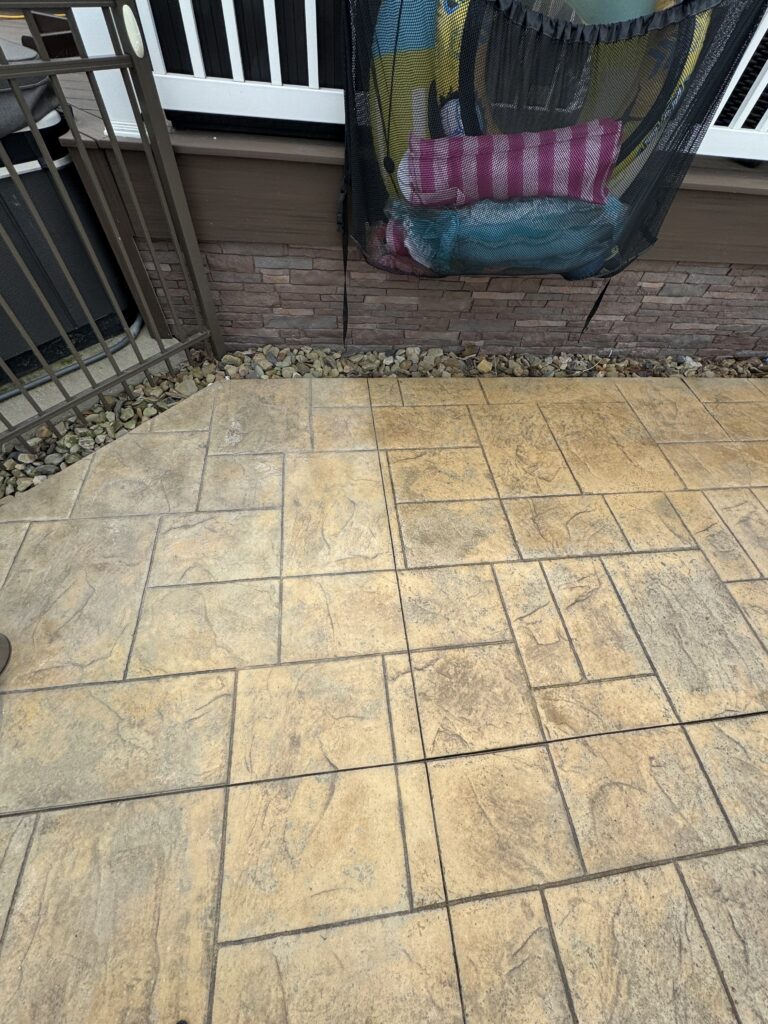 Outdoor balcony with beige tiled floor and a black mesh hanging chair filled with colorful towels against a brick wall.