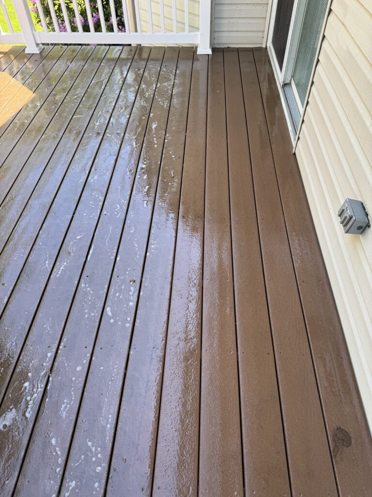 Wet brown wooden deck with water spots, white railing on the left, and a sliding glass door to a beige house exterior.