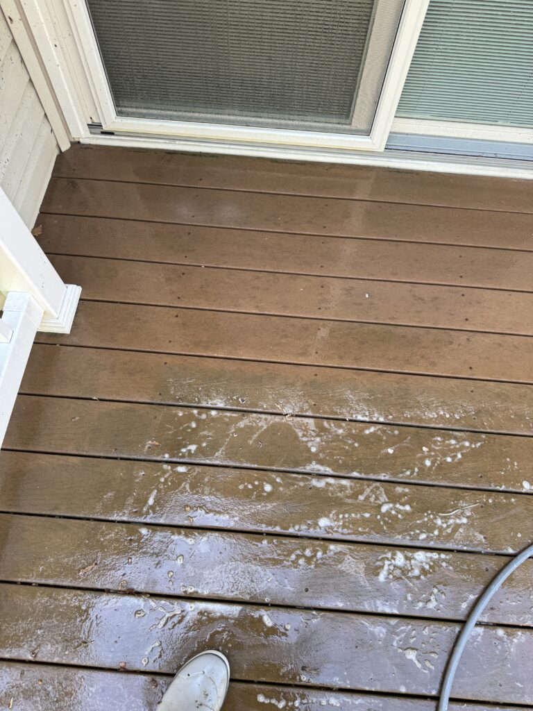 Wet brown wooden deck outside a sliding glass door with soapy splashes; a gray shoe is visible in the foreground.