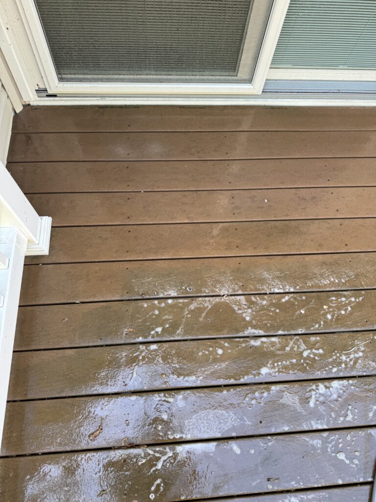 Brown wooden deck outside a sliding glass door, wet with soap suds and scattered dirt spots.]
