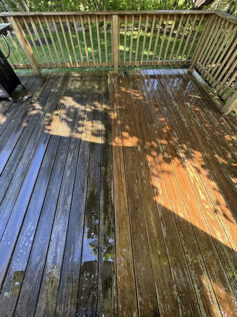 Wet wooden deck with vertical railing, dappled sunlight and leaf shadows, outdoors in a backyard garden.
