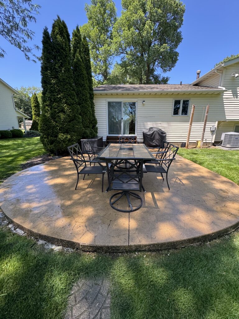 Backyard patio with a metal dining set on a circular concrete surface beside a sliding-glass door.