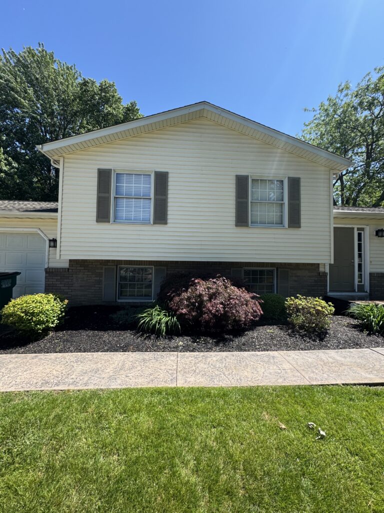 Front view of a two-story suburban house with beige siding, gray shutters, and a manicured yard.