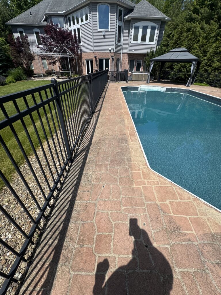 Backyard with an in-ground pool, brick patio, and black metal fence beside a gray siding home with a gazebo in the background.