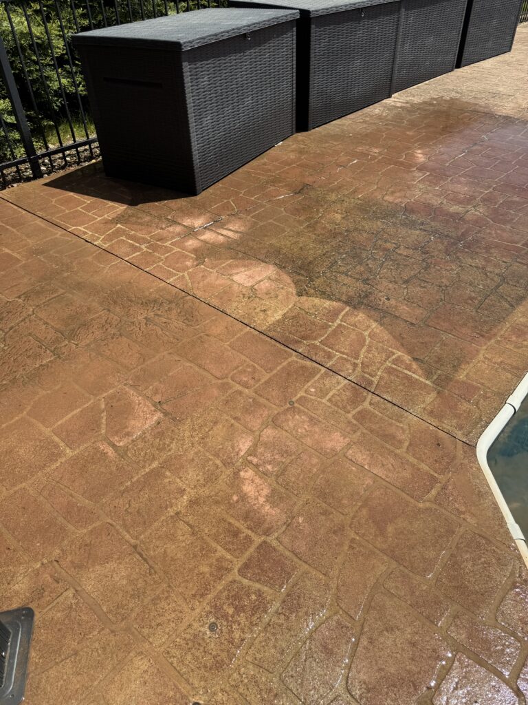 Dark wicker storage boxes along a black fence on a wet brown stamped-concrete patio.